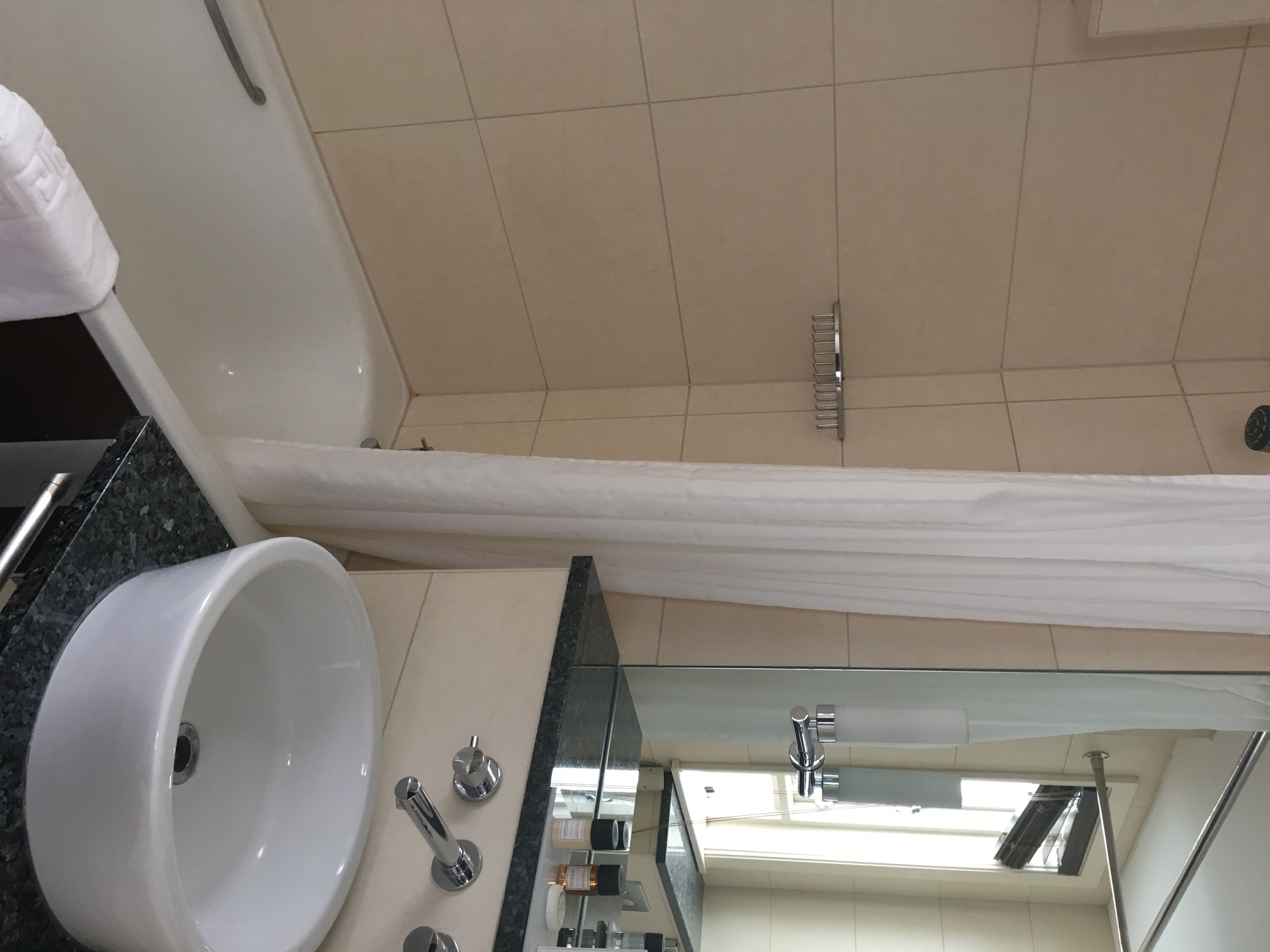 A modern bathroom with a white sink, a mirror, and a shower curtain.