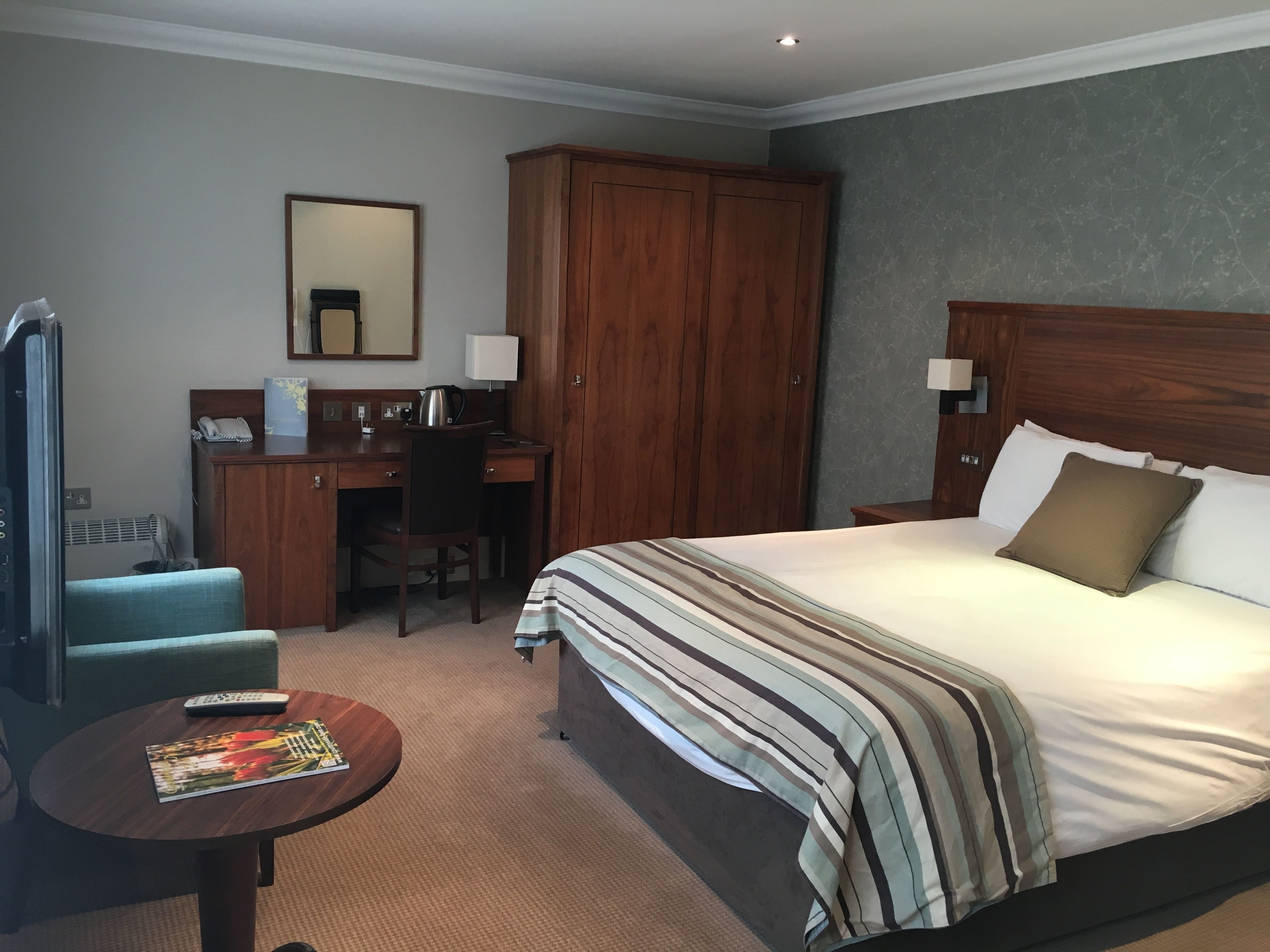 A hotel room with a bed, a desk, a chair, a round table, and a wardrobe.