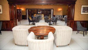 Eine geräumige Lobby mit einem runden Holztisch, umgeben von gepolsterten Sesseln, einer Couch und einem Kamin.