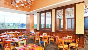 Un comedor con varias mesas y sillas, ventanas amplias y un elegante candelabro.