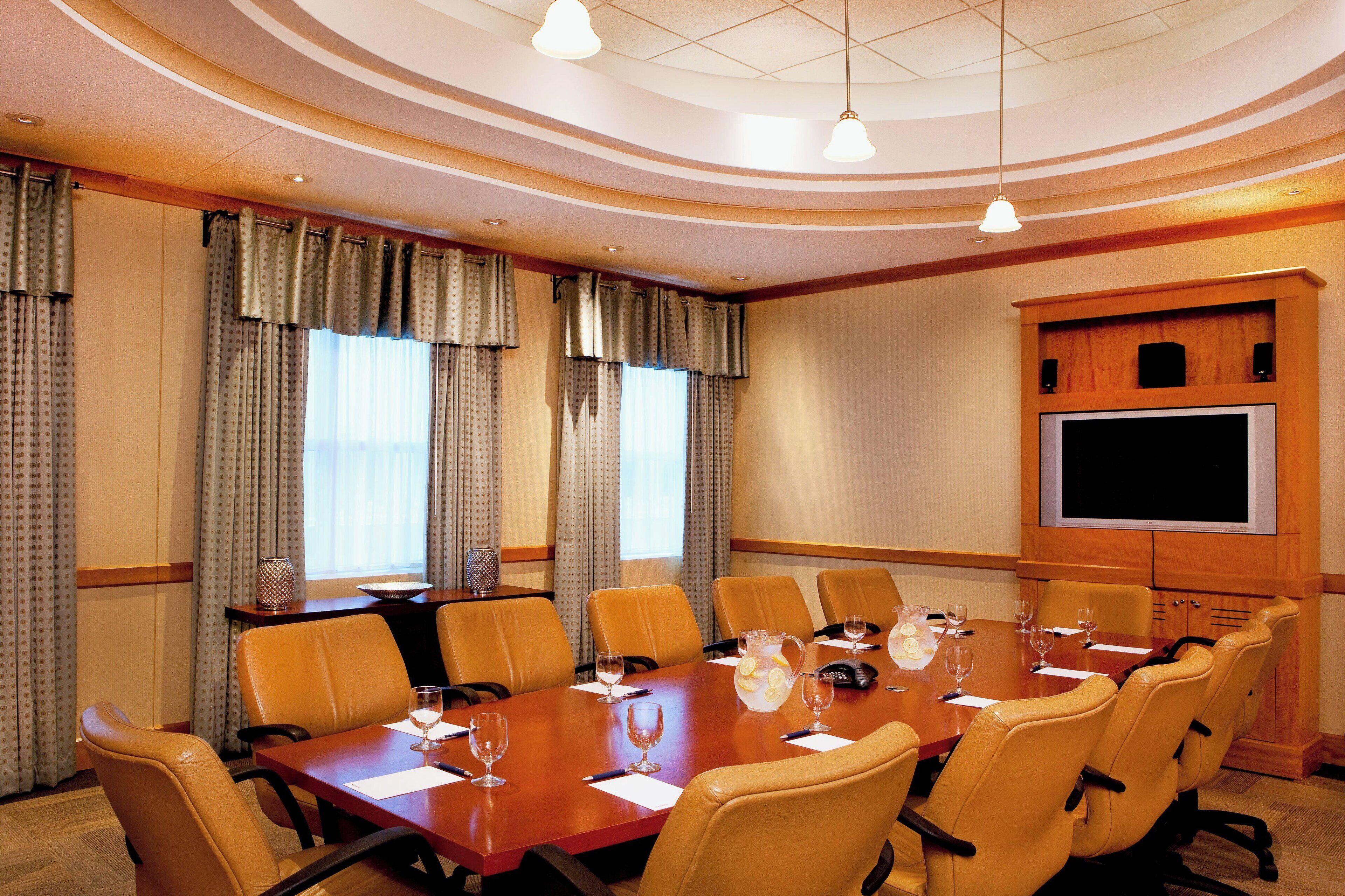 A conference room with a long table, multiple chairs, a projector screen, and a large window with curtains.