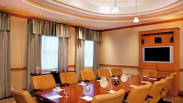 A conference room with a long table, multiple chairs, a projector screen, and a large window with curtains.