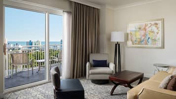 Habitación de hotel con un balcón grande, un sofá, una silla, una mesa y un cuadro.