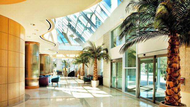 A spacious lobby with a high ceiling, large windows, and palm trees. - Sheraton Myrtle Beach (Myrtle Beach)