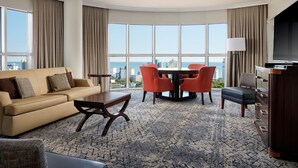 A hotel room with a large window, a sofa, a dining table with chairs, a TV, and a dresser. - Sheraton Myrtle Beach (Myrtle Beach)