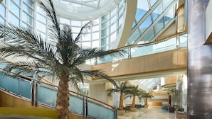 A spacious atrium with a high ceiling, glass railings, and palm trees. - Sheraton Myrtle Beach (Myrtle Beach)