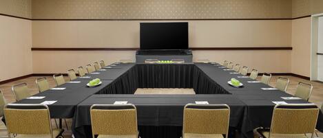 Une salle de conférence équipée d’une longue table, de chaises, d’un écran et d’un projecteur.