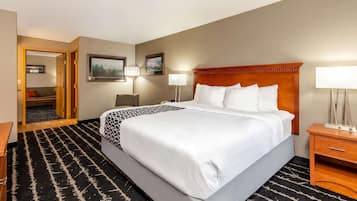 A hotel room with a large bed, a wooden headboard, two bedside tables with lamps, a black and white patterned rug, and a door leading to another room.