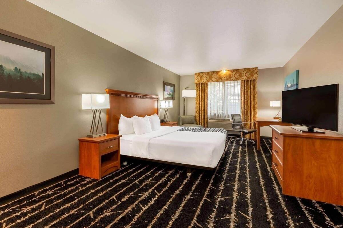 Ein Hotelzimmer mit einem großen Bett, einem Schreibtisch mit Fernseher, einem Sessel und einer Schreibtischlampe.