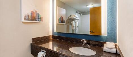 A bathroom with a granite countertop, a white sink, a mirror, and a towel rack.