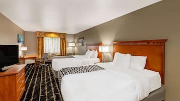 Quarto de hotel com duas camas, uma mesa, uma televisão e uma janela grande com cortinas.