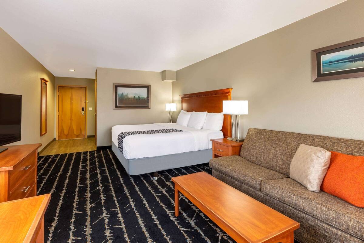 Ein Hotelzimmer mit Bett, Sofa, Fernseher, Schreibtisch und Teppichboden.
