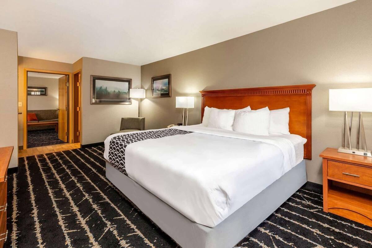 Ein Hotelzimmer mit einem großen Bett, einem Holzkopfteil, zwei Nachttischlampen, einem Schreibtisch und einem Stuhl.
