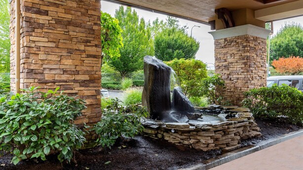 A stone fountain with water cascading down, surrounded by lush greenery and a stone wall. - La Quinta Inn & Suites by Wyndham Vancouver (Vancouver)