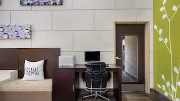 A hotel room with a bed, a desk with a computer, a chair, and a door.
