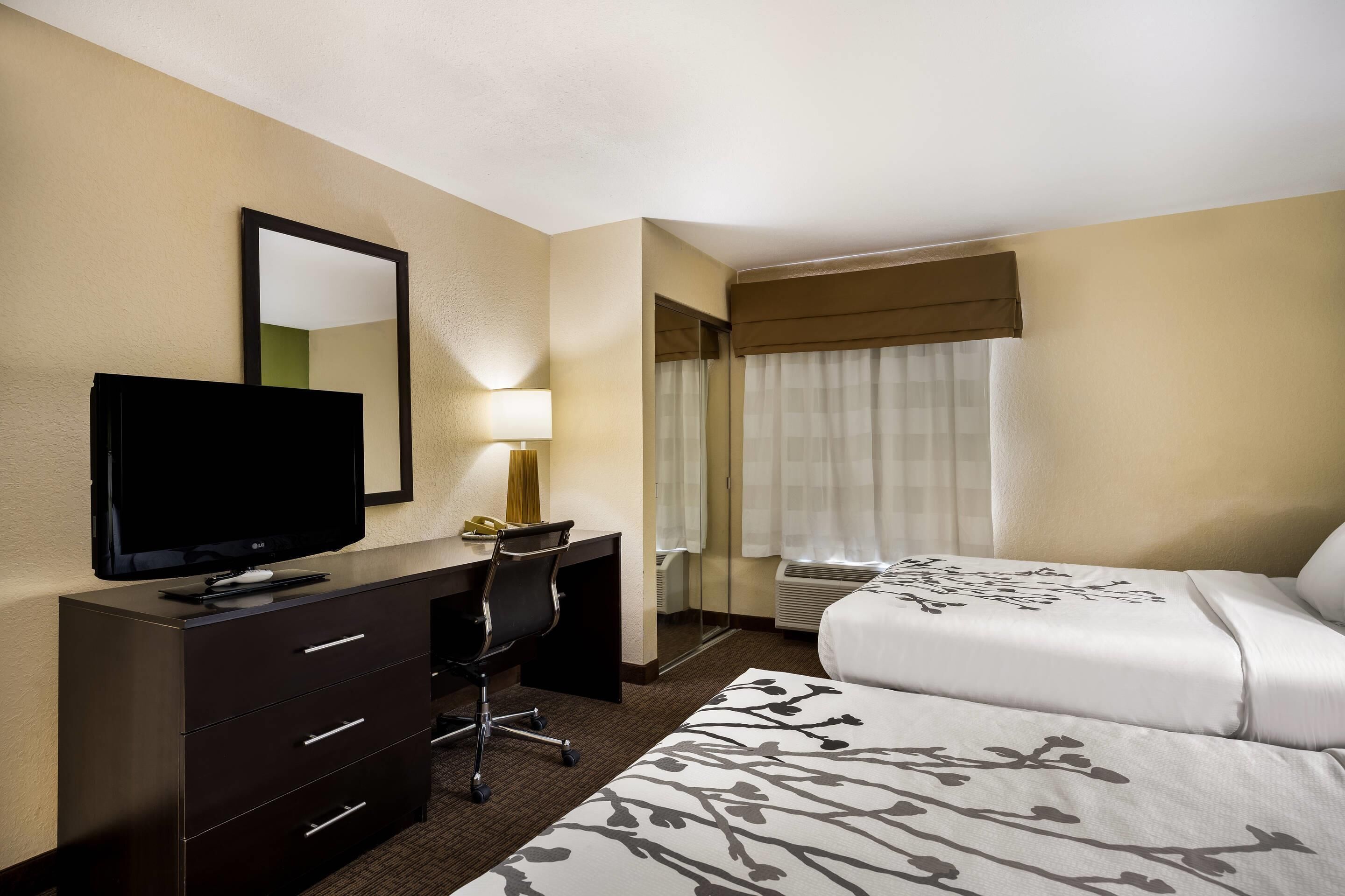 A hotel room with a bed, a desk with a TV, a chair, and a window with curtains.