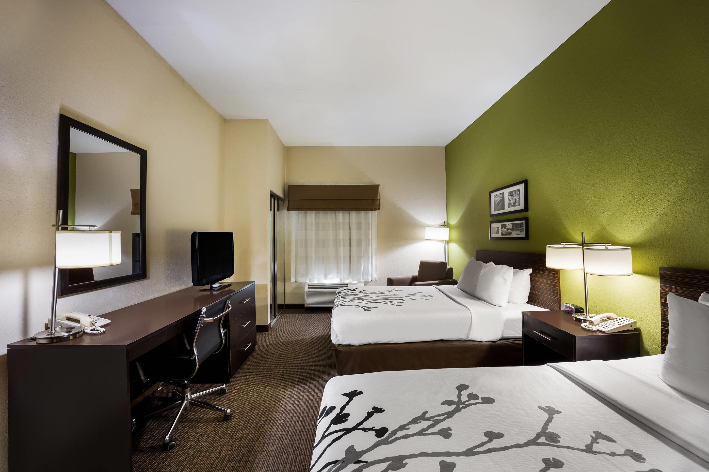 A hotel room with two beds, a desk with a telephone, a chair, a television, and a window with curtains.