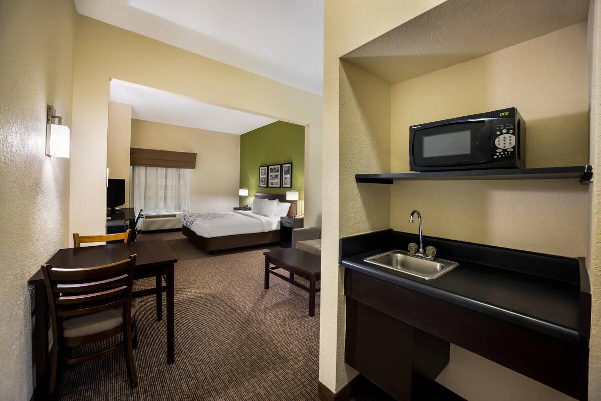 A hotel room with a bed, a desk, a chair, a microwave, and a sink.