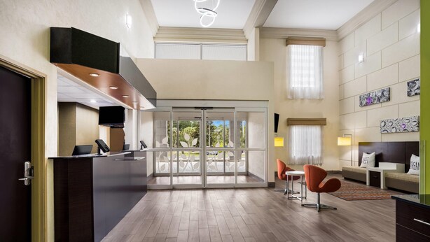 A modern hotel lobby with a reception desk, seating area, and large glass doors leading to an outdoor space. - Sleep Inn & Suites Valdosta Mall Area (Valdosta)