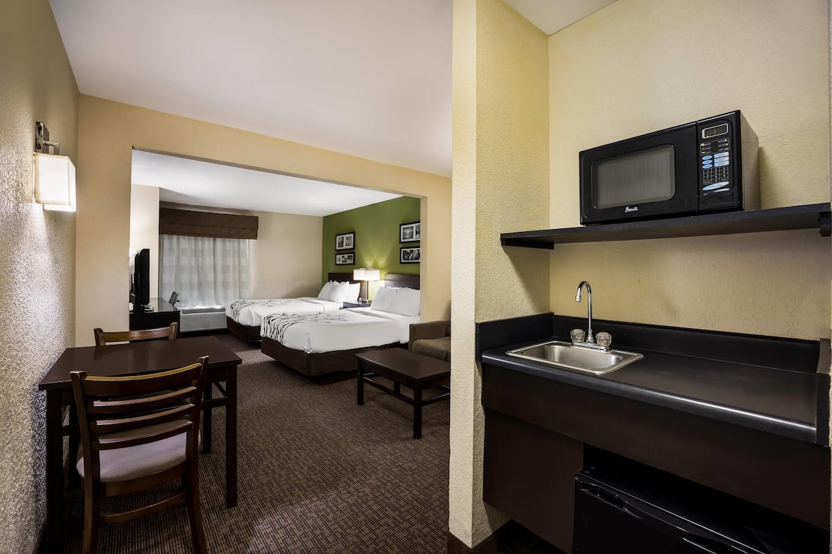 A hotel room with a kitchenette, a bed, a desk, and a chair.