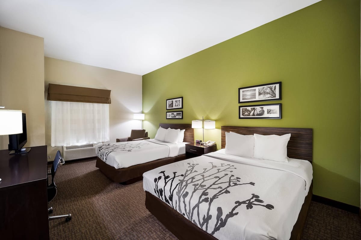 A hotel room with two beds, a desk, a chair, a TV, and a window with curtains.