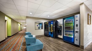 A hotel hallway with a carpeted floor, blue seating, vending machines, and a mirror. - Sleep Inn & Suites Valdosta Mall Area (Valdosta)