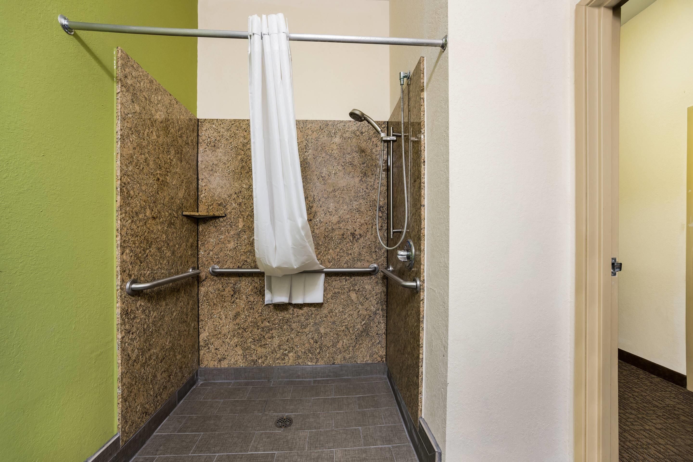 A wheelchair-accessible shower with a grab bar, a white towel hanging on the wall, and a showerhead.