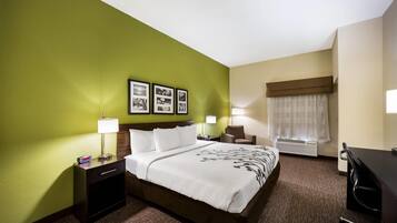 Habitación de hotel con una cama grande, un escritorio, una silla, una mesita de noche, una lámpara, una ventana con cortinas y cuadros en la pared.