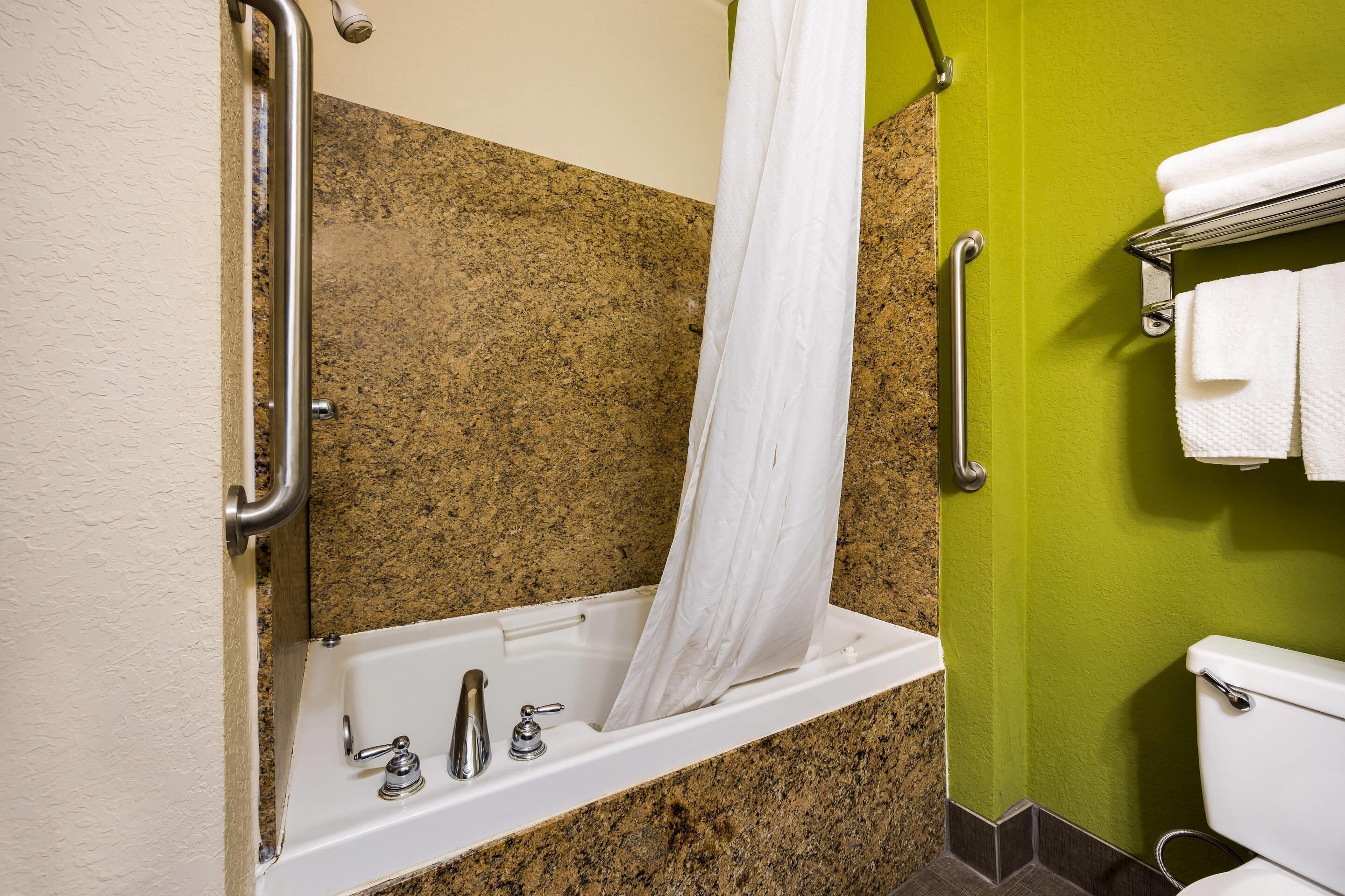 A bathroom with a bathtub, grab bars, a toilet, and a towel rack.