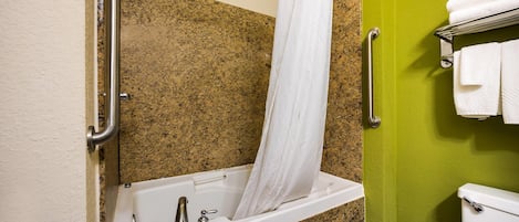 A bathroom with a bathtub, grab bars, a toilet, and a towel rack.