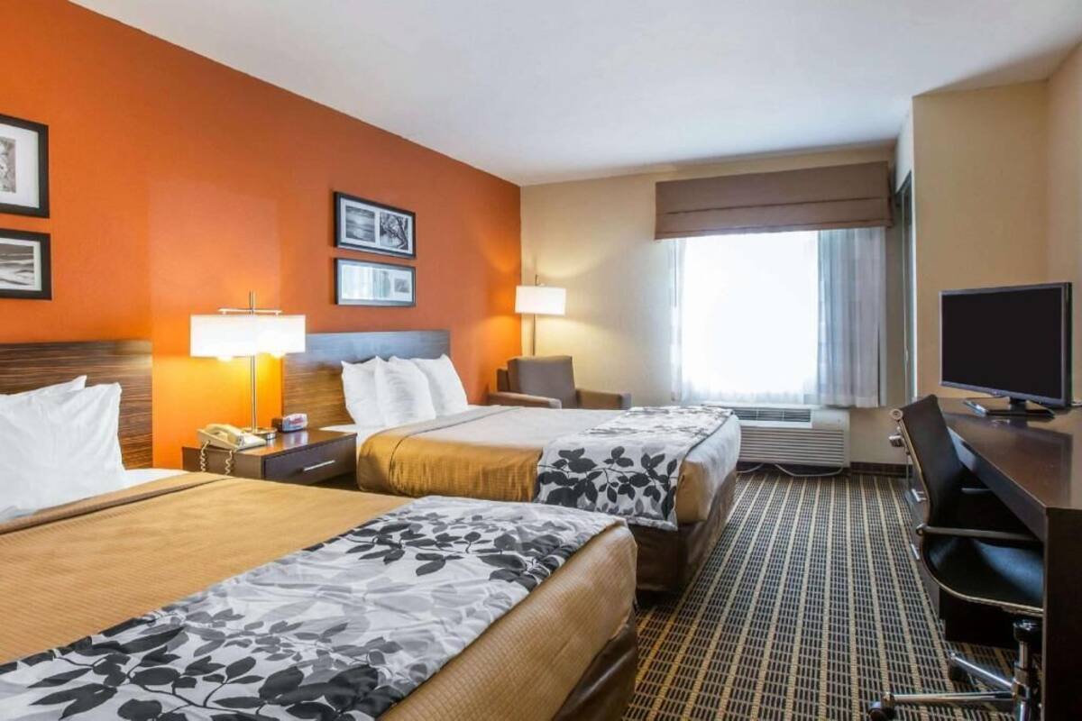 A hotel room with two beds, a desk, a TV, and a window with curtains.