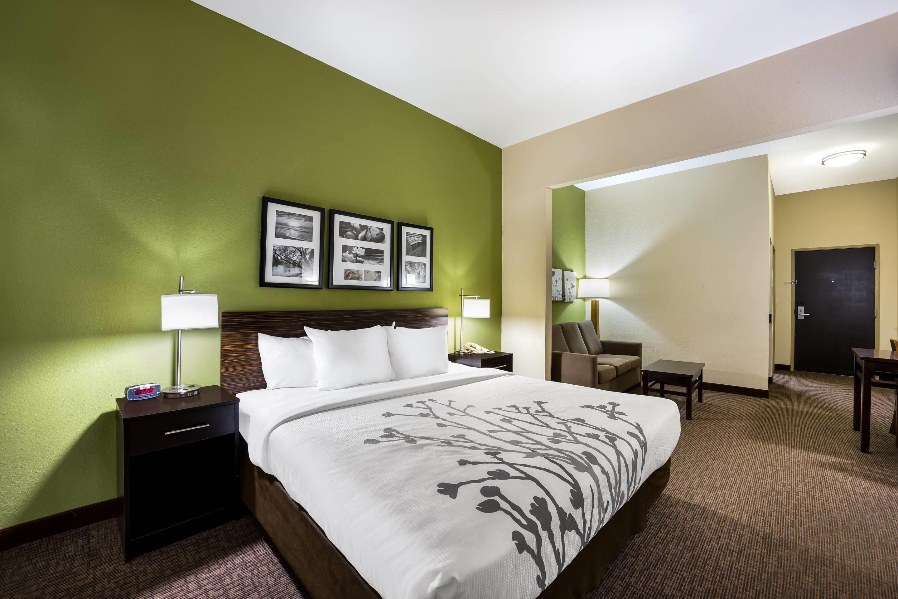 Una habitación de hotel con una cama grande, dos mesitas de noche con lámparas, una silla, un escritorio y una puerta.