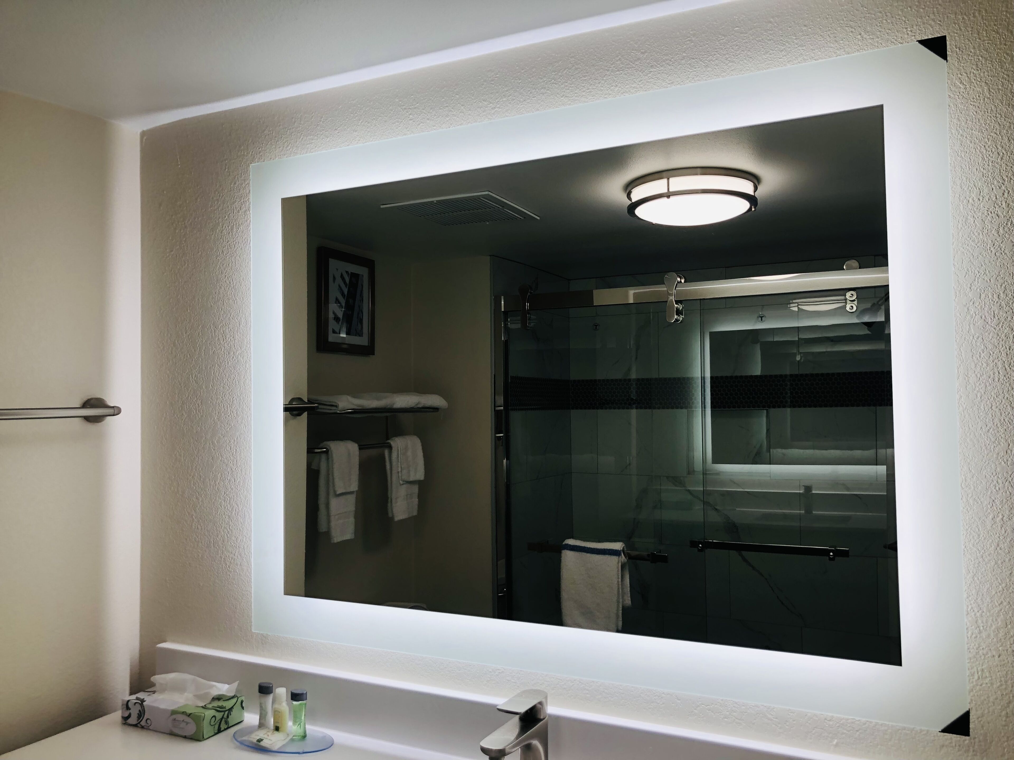 A bathroom with a large mirror, a towel rack, and a shower area.