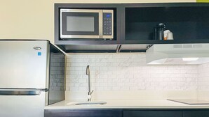 A compact kitchen with a built-in microwave, a stainless steel refrigerator, a sink, and black cabinets. - Quality Inn & Suites Lake Charles South (Lake Charles)