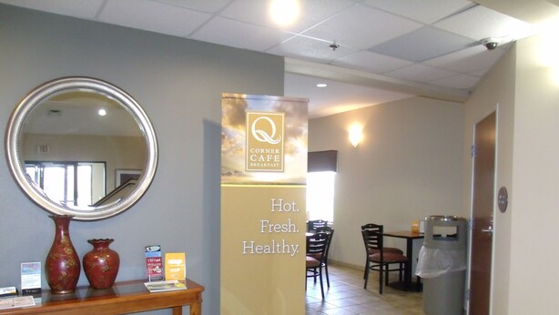 A hotel lobby with a reception desk, a mirror, a banner advertising a cafe, and a trash can. - Quality Inn & Suites Lake Charles South (Lake Charles)