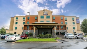 Ein Sleep Inn Hotel mit Steinfassade, mehreren Balkonen und einem Parkplatz mit einigen Autos.