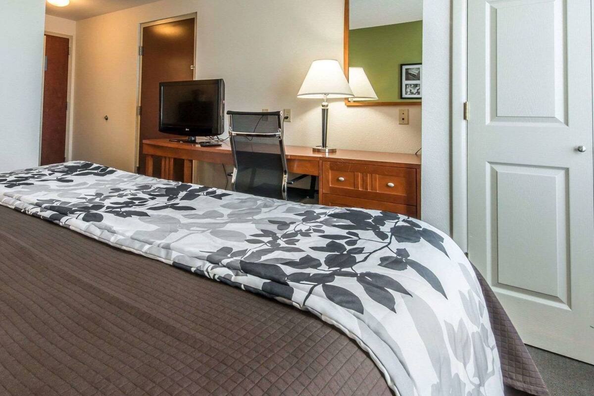 A hotel room with a bed, a desk with a computer and lamp, a television, and a door.