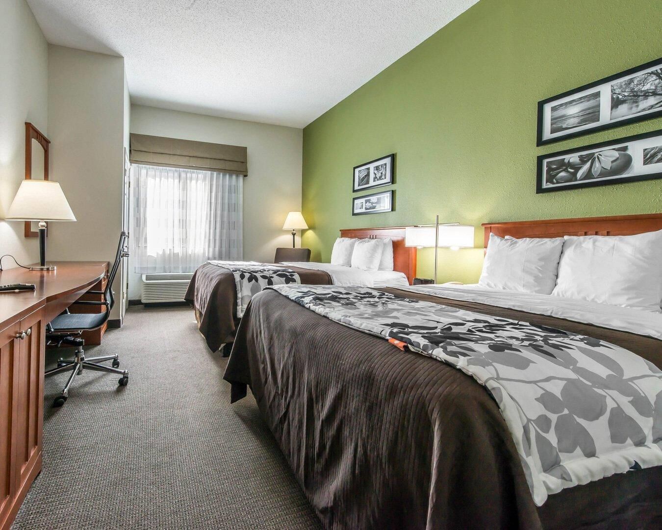 Een hotelkamer met twee bedden, een bureau met stoel, een lamp en ingekaderde foto's aan de muur.