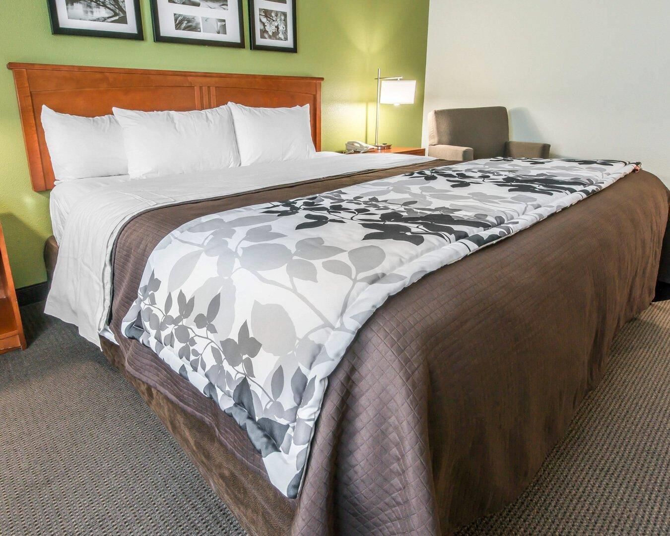 Una cama bien hecha con una colcha de estampado floral, un cabecero de madera, una lámpara de noche y una silla.