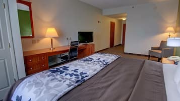 Una habitación de hotel con una cama grande, un escritorio con televisor, una silla y una lámpara.