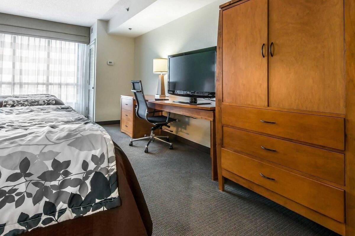 A hotel room with a bed, a desk with a computer and TV, a wardrobe, and a window with blinds.