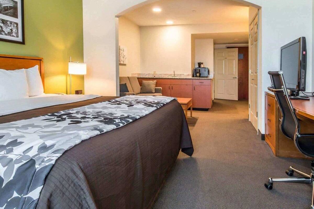 A hotel room with a bed, desk, chair, and kitchenette.