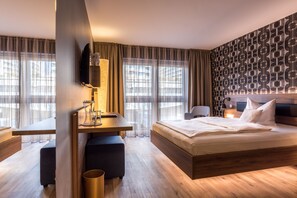 Una habitación de hotel moderna con una cama de madera, un escritorio y un ventanal con cortinas.