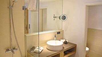 Un bany amb box de dutxa de vidre, un lavabo amb mirall i un vàter.