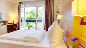 Habitación de hotel con cama, escritorio, silla, televisor y ventana con cortinas.