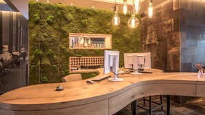 A reception desk with a curved design, a wooden chair, a computer monitor, and a vase with flowers. - Bavaria Boutique Hotel (Munich)
