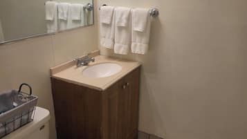 Un baño pequeño con inodoro, lavamanos y espejo. Hay tres toallas blancas colgadas en un perchero.