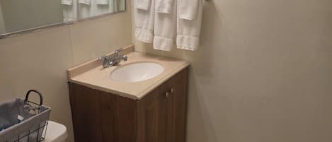 A small bathroom with a toilet, sink, and mirror. There are three white towels hanging on a towel rack.