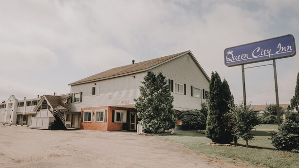 A Queen City Inn with a prominent sign, a brick office building, and a large lawn area.