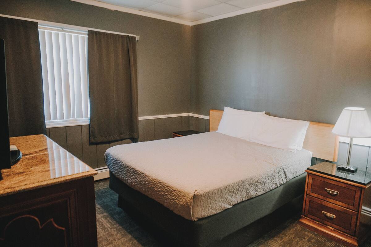 A hotel room with a bed, bedside table, lamp, and a window with curtains.